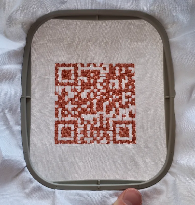 A working QR code embroidered in rust-coloured thread on linen